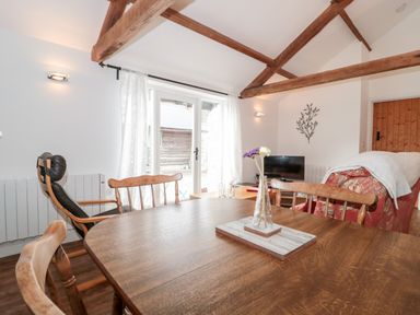 A dining room with wooden table and chairs a recliner and a sofa facing a television at Snowdrop Cottage in Llantwit Major