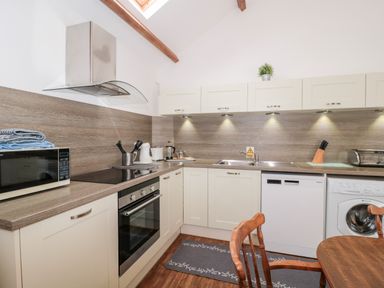 A kitchen with cream cabinets wooden countertops a microwave oven dishwasher washing machine and wooden chairs at Snowdrop Cottage in Llantwit Major