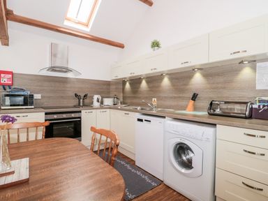 A kitchen with wooden table and chairs white cabinets and appliances at Snowdrop Cottage in Llantwit Major