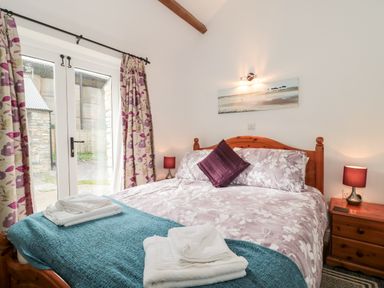 A bedroom with a double bed bedside tables and lamps next to glass doors with floral curtains at Snowdrop Cottage in Llantwit Major