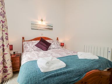 A bedroom with a wooden bed with folded towels on a blue blanket at Snowdrop Cottage in Llantwit Major