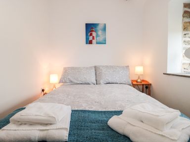 A bedroom with a bed folded towels two lamps on wooden bedside tables and a lighthouse picture on the wall at Snowdrop Cottage in Llantwit Major