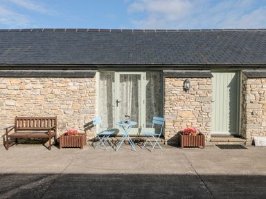 A stone wall cottage exterior with a wooden bench two blue chairs and a blue table with coffee at Snowdrop Cottage in Llantwit Major