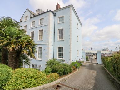 A blue multi-story building with white window frames beside a driveway with greenery and palm trees at Dawn Catcher in Falmouth