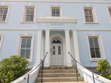 The front entrance of a blue building with white columns and steps with plants on either side at Bank House