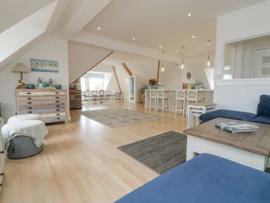 An open plan living space with wooden flooring blue sofa dining table and kitchen bar with stools at Dawn Catcher in Falmouth