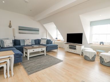 A living room with a large blue sectional sofa cushions coffee table television and windows at Dawn Catcher in Falmouth