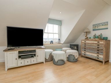 A room with a television on a cabinet a window with bins covered with cloth a chest of drawers with a lamp and decorative items at Dawn Catcher in Falmouth