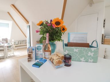 A kitchen counter with a bouquet of flowers bottles of biscuits scones jam and a fabric basket at Dawn Catcher in Falmouth