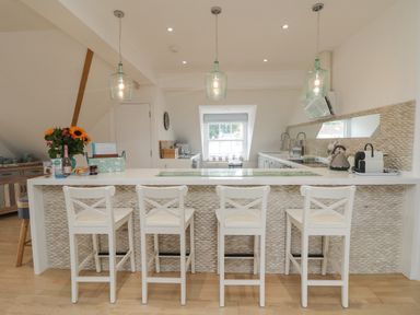 A kitchen with a white island and four white chairs with pendant lights above at Dawn Catcher in Falmouth