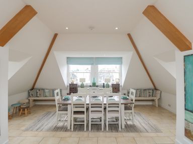 A dining room with a wooden table and white chairs set with plates and bowls at Dawn Catcher in Falmouth