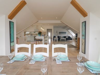 A dining table set with plates and glasses overlooking a kitchen and living area in an open-plan room at Dawn Catcher in Falmouth