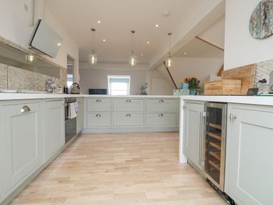 A kitchen with light grey cabinets wooden floor and pendant lights at Dawn Catcher in Falmouth