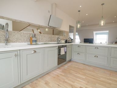 A kitchen with light gray cabinets a built in oven a long rectangular mirror a countertop with a sink and kitchen utensils at Dawn Catcher in Falmouth