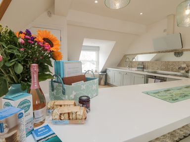 A kitchen with light blue cabinets a white countertop a window and flowers with food items on the counter at Dawn Catcher in Falmouth