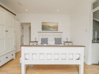 A bedroom with a white bed frame two bedside tables lamps a wardrobe and a painting above the bed at Dawn Catcher in Falmouth