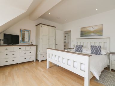 A bedroom with a white bed frame dresser wardrobe television and painting above the bed at Dawn Catcher in Falmouth
