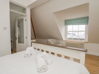A bedroom with a white bed and rolled towels near a window with a view of the sea and ships at Dawn Catcher in Falmouth