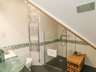A bathroom with a glass sink a toilet a heated towel rail and a glass shower enclosure at Dawn Catcher in Falmouth