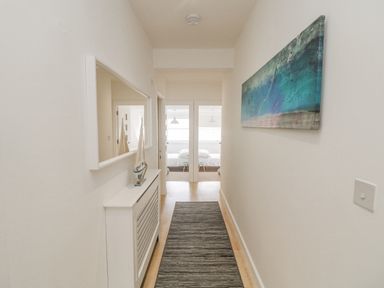A hallway with a rug a cabinet with a model sailboat a mirror and a painting with doors leading to bedrooms at Dawn Catcher in Falmouth