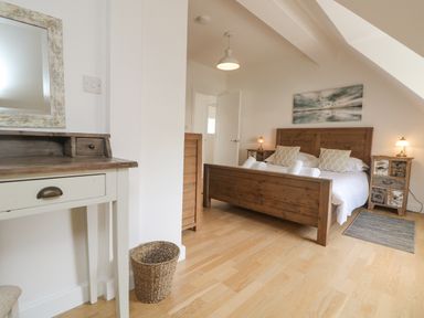 A bedroom with a wooden bed and matching bedside tables two lamps a dressing table with a mirror and a wicker basket at Dawn Catcher in Falmouth