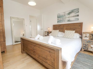 A bedroom with a wooden bed frame white bedding two pillows bedside tables with lamps a standing mirror and a painting on the wall at Dawn Catcher in Falmouth