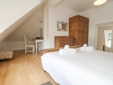 A bedroom with a wooden bed and white linens wooden wardrobe and chest of drawers a white chair and desk with a mirror at Dawn Catcher in Falmouth