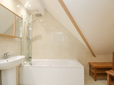 A bathroom with a bathtub a shower a sink a mirror and a wooden bench at Dawn Catcher in Falmouth