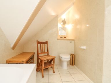 A bathroom with a toilet wooden chair wooden bench and a small mirror on tiled walls at Dawn Catcher in Falmouth