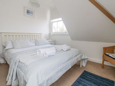 A bedroom with a bed with pillows and rolled towels near a window and a wicker chair with a cushion at Dawn Catcher in Falmouth