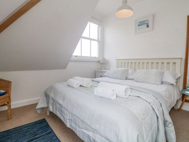 A bedroom with a double bed rolled towels bedside table and a chair at Dawn Catcher in Falmouth