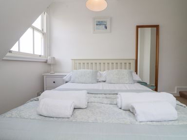 A bedroom with a bed with folded towels on it a bedside table with a lamp and a full length mirror at Dawn Catcher in Falmouth