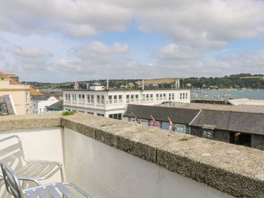 A balcony with two metal chairs overlooking buildings and boats on the water at Dawn Catcher in Falmouth