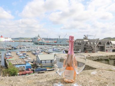 A bottle of prosecco and two wine glasses on a stone ledge overlooking a harbor with boats and buildings at Dawn Catcher in Falmouth