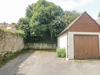 An outdoor area with a single garage door and a driveway surrounded by a stone wall and dense greenery at Dawn Catcher in Falmouth