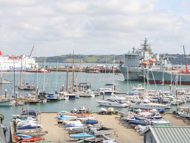 A harbor with many sailboats and a large ship with lifeboats near the shore with hills in the background at Dawn Catcher in Falmouth