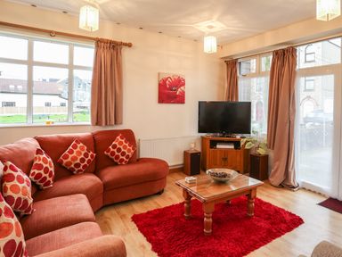 A living room with a red sectional sofa red cushions a wooden coffee table and a television at The Cabin in Combe Martin