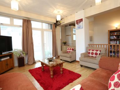 A living room with a red rug wooden coffee table couches armchairs a bookshelf and a TV at The Cabin in Combe Martin
