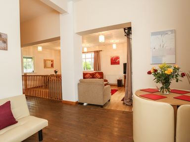 A living area with beige sofa red cushions round dining table with flowers and cream chairs at The Cabin in Combe Martin