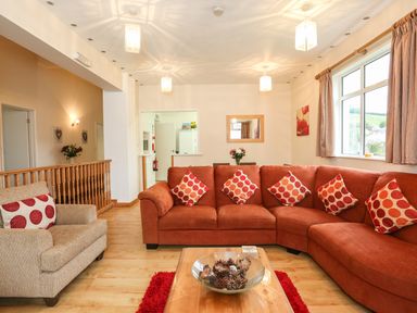 A living room with an orange sectional sofa and patterned cushions a beige armchair and a wooden coffee table with a glass bowl at The Cabin in Combe Martin