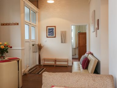 A sitting area with a small sofa and cushions next to a doorway with wooden furniture in the adjacent room at The Cabin in Combe Martin