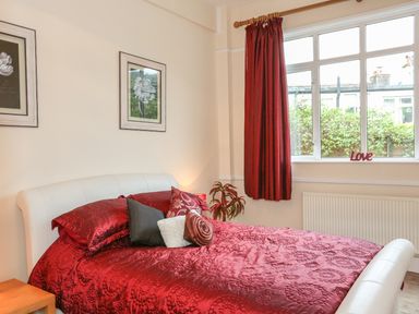 A bedroom with a white bed frame red bedding red curtains and framed pictures on the wall at The Cabin in Combe Martin