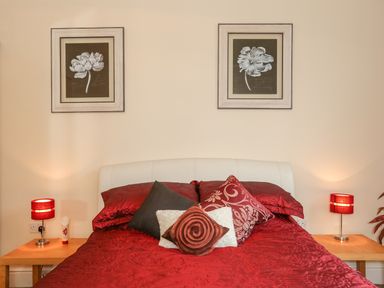 A bedroom with a bed with red bedding two bedside tables with red lamps and floral pictures on the wall at The Cabin in Combe Martin