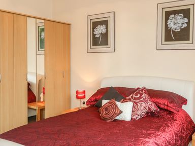 A bedroom with a bed with red bedding and pillows a wooden wardrobe with mirrors and two flower pictures on the wall at The Cabin in Combe Martin