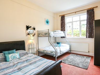 A bedroom with a double bed, bunk bed, bedside table with lamp, window with curtains, and a rug on the floor at The Cabin in Combe Martin