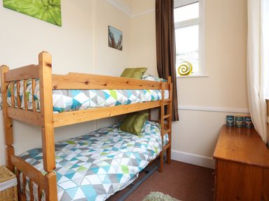 A small bedroom with wooden bunk beds patterned bedding and a wooden dresser with three jars on top at The Cabin in Combe Martin