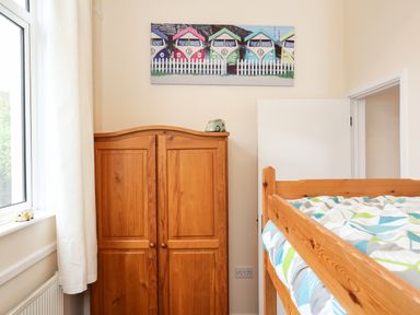 A bedroom with a wooden wardrobe, bunk bed, window with curtains, and wall art with colorful camper vans at The Cabin in Combe Martin