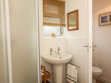 A bathroom with a pedestal sink mirror towel and window with blinds at The Cabin in Combe Martin