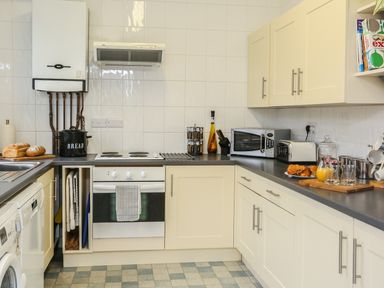 A kitchen with white cabinets a stove microwave toaster and countertop items at The Cabin in Combe Martin