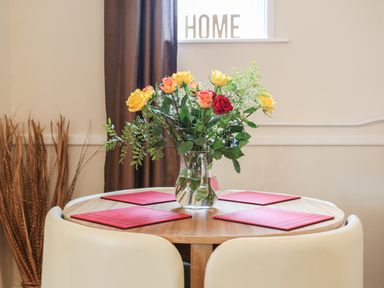 A dining table with a glass vase of flowers and red placemats with white chairs at The Cabin in Combe Martin